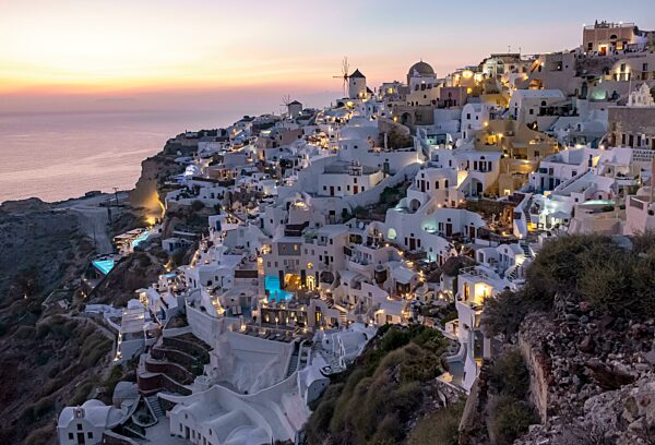 Klippenhäuser, Villen und Windmühle im Dorf Ia von der Burg Oia aus gesehen in der Abenddämmerung, Santorin, Griechenland, Europa