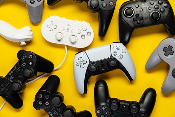 Verschiedene Generationen Gamecontroller der Playstation und Nintendo Spielekonsole, vor einfarbig gelben Hintergrund, top view