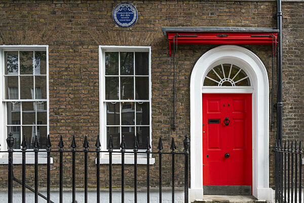 Rote Eingangstür in einem Backsteingebäude mit einem gußeisernen Zaun...