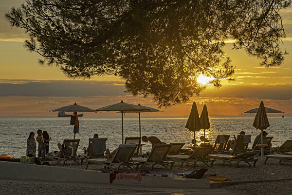 Touristen am Strand in Liegestühlen genießen den Sonnenuntergang über der...