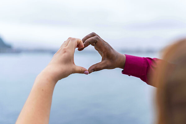 Braut und Bräutigam bilden mit ihren Händen eine Herzform vor einer...