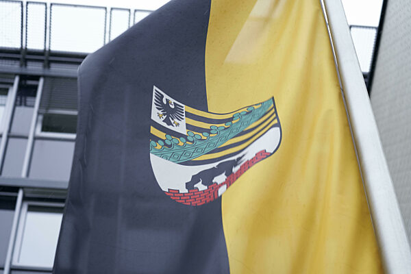 Wehende Fahne mit Wappen des Bundeslandes Sachsen-Anhalt vor Gebäude des...