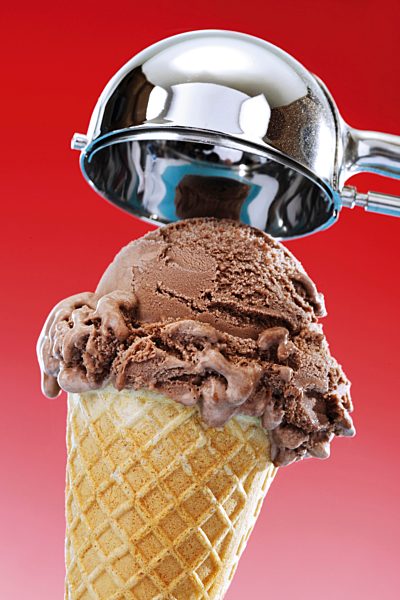 Eine Kugel Schokoeis in Waffeltüte, darüber ein Eisportionierer