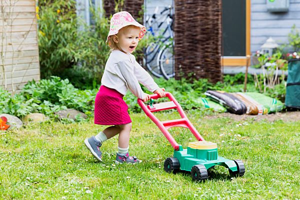 Little girl in the garden with toy lawn mower