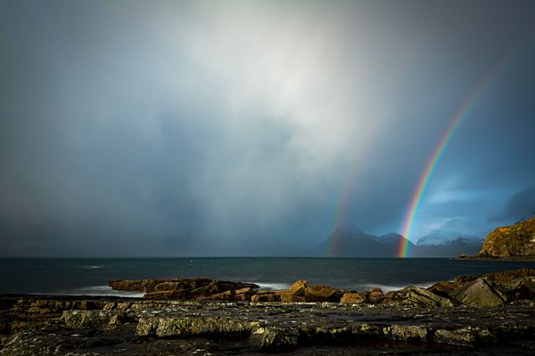 Große Felsen im Wasser der Nordsee mit verschneiten Cullin Bergen und Regenbogen im Hintergrund, Elgol, Isle of Skye, Schottland, Großbritannien, Europa