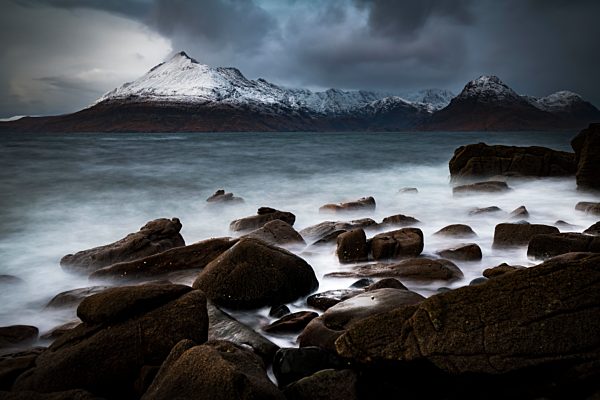 Große Felsen im Wasser der Nordsee mit verschneiten Cullin Bergen im Hintergrund, Elgol, Isle of Skye, Schottland, Großbritannien, Europa