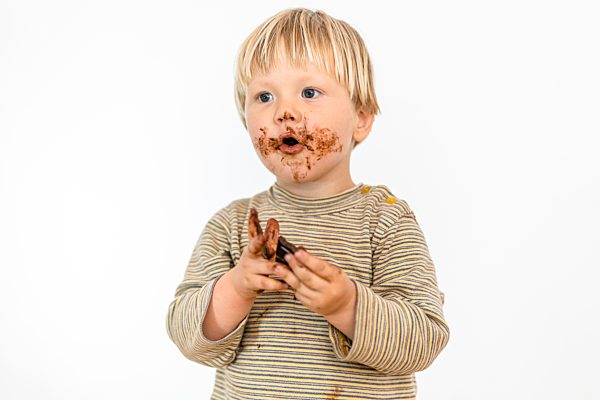 Süßes blondes Kleinkind isst mit großer Freude Schokoladentafel, weißer Hintergrund, Polen, Europa