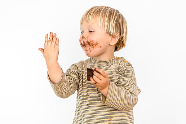Süßes blondes Kleinkind isst mit großer Freude Schokoladentafel, weißer Hintergrund, Polen, Europa