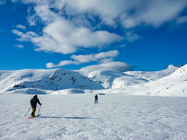 Zwei Skitourengeher überqueren einen gefrorenen See im winterlichen Gebirge, Insel Senja, Troms, Norwegen, Europa