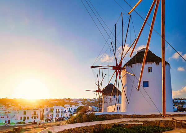 Berühmte Touristenattraktion von Mykonos, Kykladen, Griechenland. Drei traditionelle weiß getünchte Windmühlen in einer Reihe gegen die aufgehende Sonne über Chora, Hauptort der Insel. Sommer, Sonnenaufgang, Morgen, blauer Himmel, Wolken. Reiseziel, i