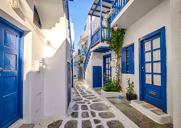 Klassische und traditionelle enge Straßen, schöne Gassen der griechischen Inselstädte. Weiß getünchte Häuser, Blumentöpfe, blaue Balkone, Treppen und Türen, kopfsteingepflasterte Straßen. Romantischer Urlaub, Traumwochenende. Sommermorgensonne. My