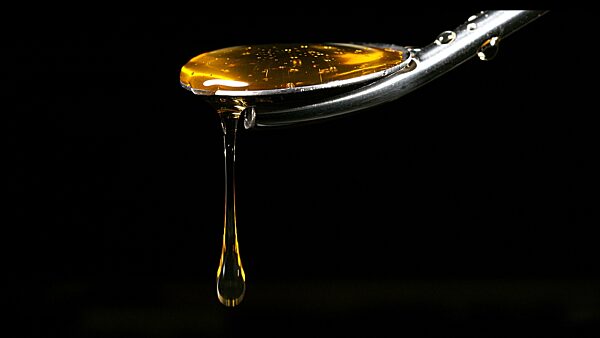 Honig fließt von Löffel gegen schwarzen Hintergrund