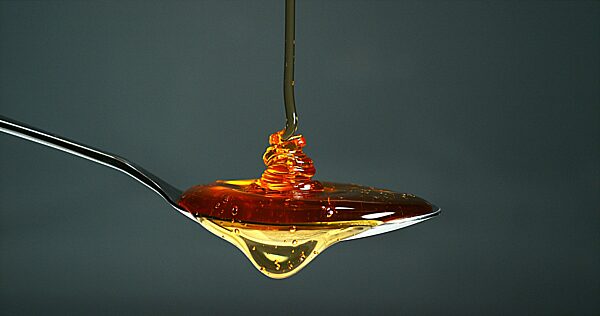 Honig fließt in einem Löffel gegen schwarzen Hintergrund