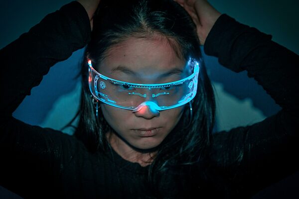 Nahaufnahme Studiofoto mit blauem Hintergrund mit Neonlichter einer chinesischen jungen Frau mit Augmented Reality Brille