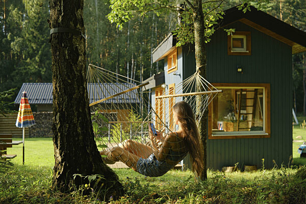 Rückansicht einer Frau, die mit ihrem Smartphone in einer Hängematte in der...