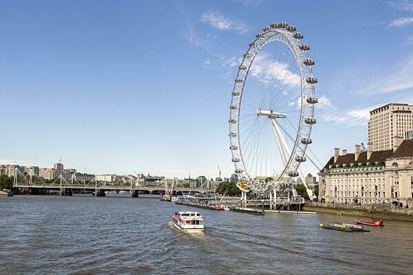Die Themse mit Booten und das Riesenrad London Eye bei blauem Himmel in...