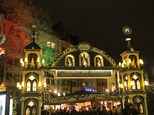 Beleuchteter Eingang eines Weihnachtsmarktes bei Nacht mit vielen Menschen...