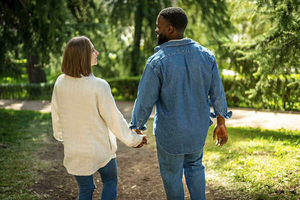 Rückansicht eines multiethnischen Paares, das händchenhaltend durch einen...
