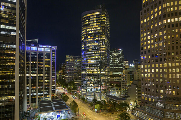 Nächtliche Stadtaufnahme mit beleuchteten Hochhäusern und Straßen im...