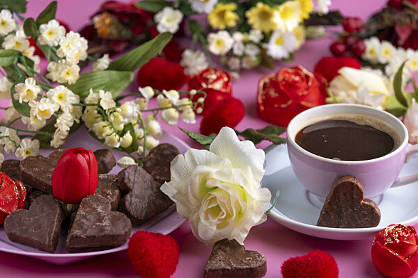 Kaffeetasse mit Schokolade und Blumenarrangement auf rosa Hintergrund...