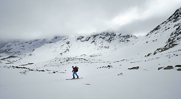 Skitourengeher in winterlicher Berglandschaft mit wolkenverhangenen...