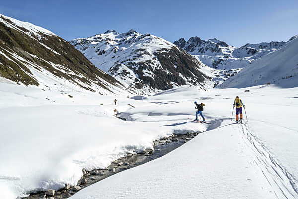 Zwei Skitourengeher im Schnee überqueren einen Bergbach im Funtauna Tal...