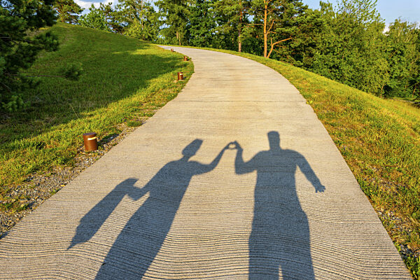 Schatten eines Paares, das auf einem Gehweg spazieren geht und mit seinen...