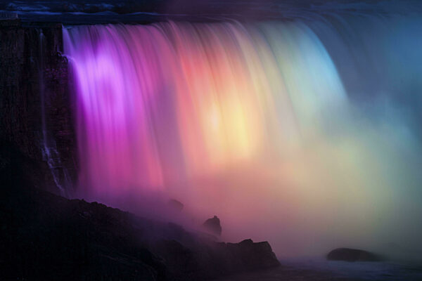 Wasserfall bei Nacht, der in leuchtenden Regenbogenfarben leuchtet und einen...