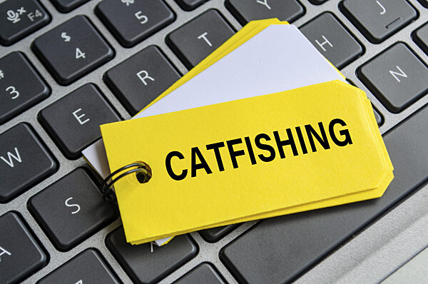 Catfishing Text auf weißem Notizblock mit Laptop Tastatur Hintergrund...