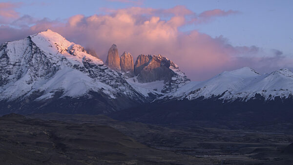 Dramatischer Sonnenuntergang über schneebedeckten Bergen mit rosa Wolken und...