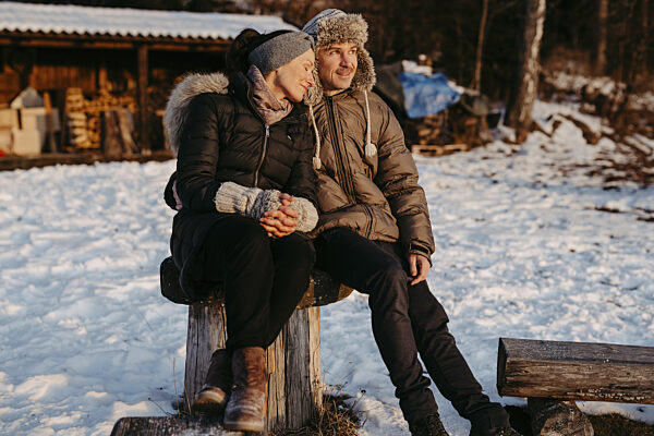 Glückliches, Paar sitzt auf Holzstamm im Schnee