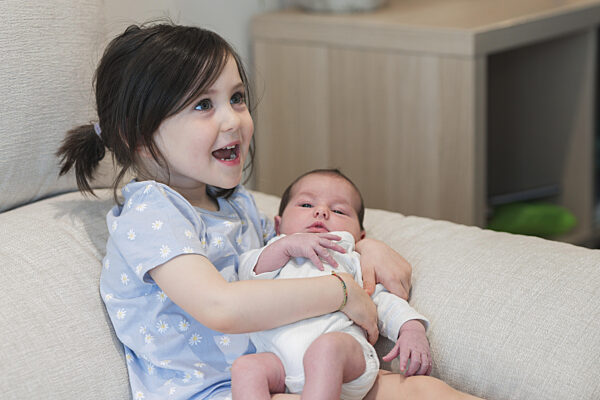 Ein fröhliches junges Mädchen hält ihr neugeborenes Geschwisterchen...
